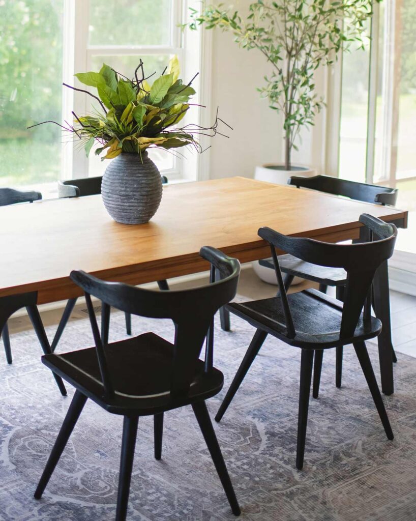 A decorative plant on a kitchen table with chairs surrounded by nice, open concept windows